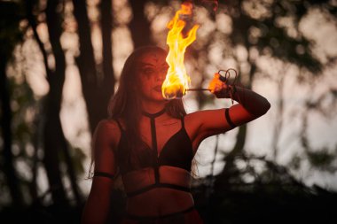 Açık hava sanat festivalinde kız ateş dansı gösterisi, meşaleli kadın ateş gösterisi sanatçısının düzgün hareketleri. Alevli dans eden kadın sanat performansı, alacakaranlık ormanı arka planı