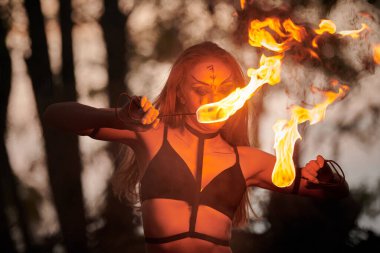 Açık hava sanat festivalinde kız ateş dansı gösterisi, meşaleli kadın ateş gösterisi sanatçısının düzgün hareketleri. Alevli dans eden kadın sanat performansı, alacakaranlık ormanı arka planı
