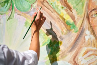 Ressam kız eli fırçayı tutuyor ve açık hava resim festivalinde tuvale yeşil doğa manzarası çiziyor, resim resim süreci. Kadın sanatçı atmosferik gerçeküstü resim çiziyor.