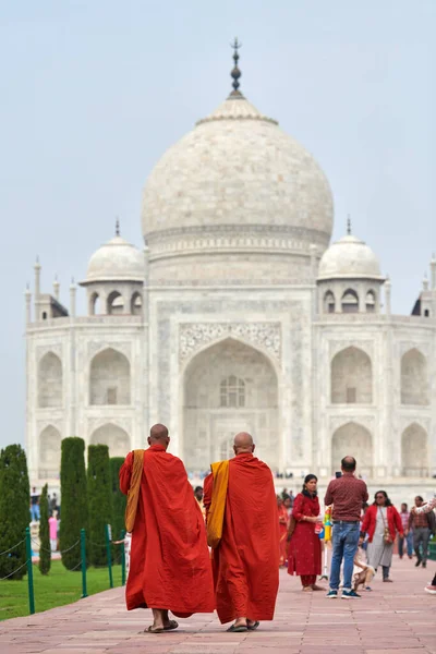 Agra, Hindistan - 09.11.2022 - Taj Mahal mermer mozolesine yürüyen kırmızı cübbe ve turuncu çantalar giyen iki Tibetli keşiş, Hindistan 'ın çok uluslu turizminde yürüyen iki kel Tibetli keşiş