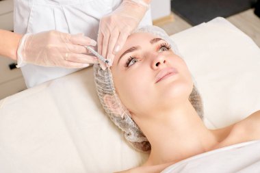 Kozmetik uzmanı kadın yüzüne gençleştirme enjeksiyonu yapıyor. Güzellik salonunda yaşlanmayı önleyen estetik cerrahi olmayan prosedür uyguluyor. Eldiven uzmanları şırınga ile iğne yapıyor.