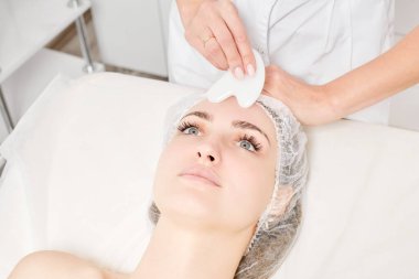 Güzellik uzmanı Gua Sha taşıyla yüz masajı yaparak güzellik salonundaki lenfatik drenaj, yaşlanmayı önleyen estetik ameliyatlar için cilde bakıyor. Gua Sha aracıyla yüz masajı