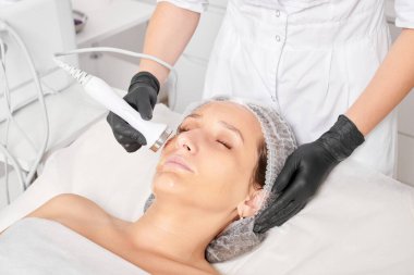 Kozmetik uzmanı, güzellik salonundaki yaşlanmayı önleyen kozmetik prosedürleri kullanarak gençleşen kadın yüzü için ultrason cildini sıkılaştırıyor. Güzellik uzmanı ultrasonik deri kaldırıyor.