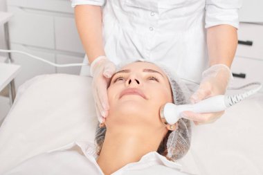 Güzellik uzmanı, güzellik salonundaki yaşlanma önleyici kozmetik işlemleri ve fonoforezi kullanarak gençleşen kadın yüzü için ultrason cildi sıkılaştırıyor. Kozmetik uzmanı ultrasonik deri kaldırıyor.