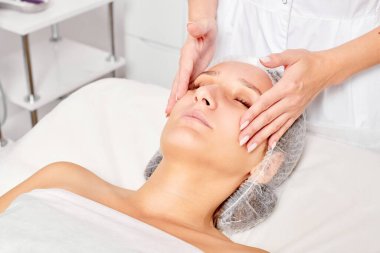 Güzellik uzmanları, güzellik salonlarında cilt bakımı, yaşlanma karşıtı estetik ameliyatlar için cilde masaj yapıyor. Güzel kadın yüzü için kozmetik kremiyle yüz masajı yapıyor.