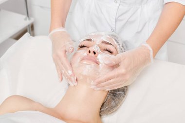 Güzellik uzmanı güzellik salonundaki nemlendirici cilt bakım için kadın yüzüne krem maskesi takıyor. Kozmetik uzmanı kadın yüzüne krem sürerken eldiven verdi.