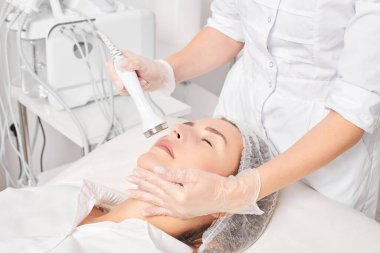 Güzellik uzmanı, güzellik salonundaki yaşlanma önleyici kozmetik işlemleri ve fonoforezi kullanarak gençleşen kadın yüzü için ultrason cildi sıkılaştırıyor. Kozmetik uzmanı ultrasonik deri kaldırıyor.