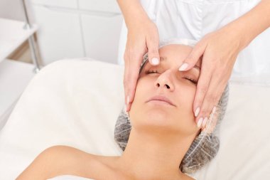 Güzellik uzmanları, güzellik salonlarında cilt bakımı, yaşlanma karşıtı estetik ameliyatlar için cilde masaj yapıyor. Güzel kadın yüzü için kozmetik kremiyle yüz masajı yapıyor.