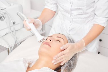 Cosmetologist makes ultrasound skin tightening for rejuvenation woman face using phonophoresis, anti aging cosmetic procedure with in beauty spa salon. Beautician makes ultrasonic skincare lifting clipart