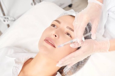 Kozmetik uzmanı güzellik salonunda dudak büyütme ve hacim için estetik cerrahi olmayan ameliyatlar yapıyor. Eldivenli güzellik uzmanı dudaklarına şırınga yapıyor.