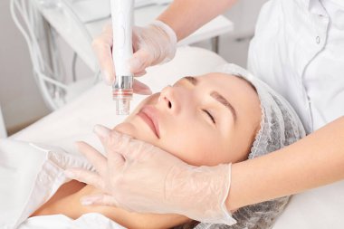Güzellik uzmanı, güzellik salonundaki yaşlanma karşıtı kozmetik prosedürü olan cilt bakımını yenilemek için su bitkisi üretiyor. Eldivenleri teslim eden kozmetolog, sıkılaştırmak için yüz bakımı yapıyor