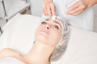 Kozmetikçiler güzellik salonundaki yüz kremi maskesini kadın yüzünden kozmetik mendillerle temizliyor, cilt yenileme estetik ameliyatları yapıyor. Güzellik uzmanları yüz maskesini çıkarmak için peçete tutuyor.