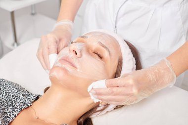 Güzellik uzmanı, güzellik salonundaki yüz kremi maskesini kadın yüzünden kozmetik mendillerle alıyor, cilt yenileme estetik ameliyatı yapıyor. Kozmetik uzmanı nemlendirici kremi peçetelerle temizliyor.