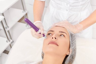 Güzellik uzmanı, gençleşen kadın yüzü için mezoterapi enjeksiyonu yapıyor. Güzellik salonunda yaşlanmayı önleyen estetik cerrahi prosedür uyguluyor. Eldivenleri teslim eden kozmetolog yüz mikro iğnesi yapıyor.