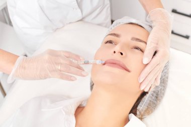 Kozmetik uzmanı güzellik salonunda dudak büyütme ve hacim için estetik cerrahi olmayan ameliyatlar yapıyor. Eldivenli güzellik uzmanı dudaklarına şırınga yapıyor.