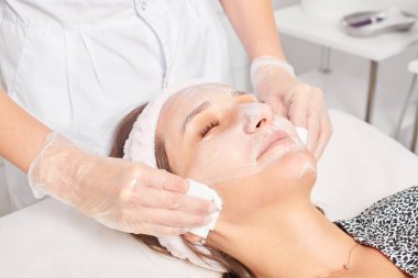 Kozmetikçiler güzellik salonundaki yüz kremi maskesini kadın yüzünden kozmetik mendillerle temizliyor, cilt yenileme estetik ameliyatları yapıyor. Güzellik uzmanı nemlendirici kremi peçeteyle kaldırıyor.