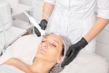Kozmetik uzmanı, güzellik salonundaki yaşlanmayı önleyen kozmetik prosedürleri kullanarak gençleşen kadın yüzü için ultrason cildini sıkılaştırıyor. Güzellik uzmanı ultrasonik deri kaldırıyor.