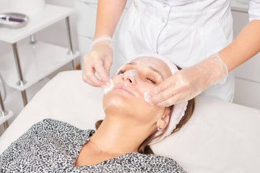 Güzellik uzmanı, güzellik salonundaki yüz kremi maskesini kadın yüzünden kozmetik mendillerle alıyor, cilt yenileme estetik ameliyatı yapıyor. Kozmetik uzmanı nemlendirici kremi peçetelerle temizliyor.