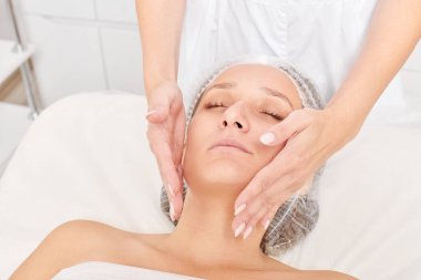 Güzellik uzmanları, güzellik salonlarında cilt bakımı, yaşlanma karşıtı estetik ameliyatlar için cilde masaj yapıyor. Güzel kadın yüzü için kozmetik kremiyle yüz masajı yapıyor.