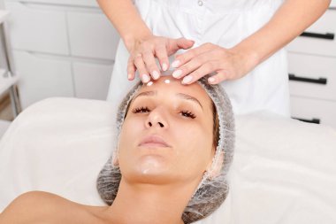 Güzellik uzmanları, güzellik salonlarında gençleştirme için nemlendirici krem maskeyi kadın yüzüne sürerler, yaşlanma karşıtı kozmetik işlemler yaparlar. Kozmetik uzmanı kadın derisi için yüz kremi uyguluyor.