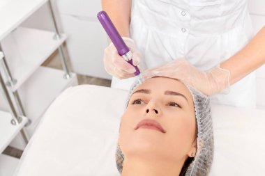 Güzellik uzmanı, gençleşen kadın yüzü için mezoterapi enjeksiyonu yapıyor. Güzellik salonunda yaşlanmayı önleyen estetik cerrahi prosedür uyguluyor. Eldivenleri teslim eden kozmetolog yüz mikro iğnesi yapıyor.