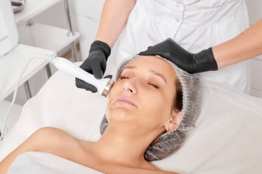 Kozmetik uzmanı, güzellik salonundaki yaşlanmayı önleyen kozmetik prosedürleri kullanarak gençleşen kadın yüzü için ultrason cildini sıkılaştırıyor. Güzellik uzmanı ultrasonik deri kaldırıyor.