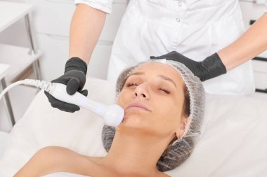 Güzellik uzmanı, güzellik salonundaki gençleştirme kadın yüzü için RF kaldırma, yaşlanma karşıtı kozmetik işlemleri yapıyor. Kozmetik uzmanı, kadın yüz derisinde artan kolajen için radyo frekansı tedavisi yapıyor.