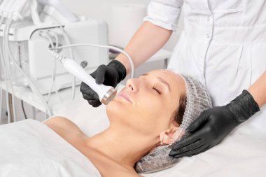 Güzellik uzmanı, güzellik salonundaki yaşlanma önleyici kozmetik işlemleri ve fonoforezi kullanarak gençleşen kadın yüzü için ultrason cildi sıkılaştırıyor. Kozmetik uzmanı ultrasonik deri kaldırıyor.