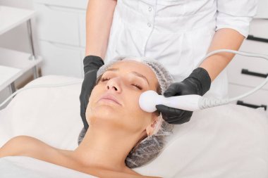 Güzellik uzmanı, güzellik salonundaki gençleştirme kadın yüzü için RF kaldırma, yaşlanma karşıtı kozmetik işlemleri yapıyor. Kozmetik uzmanı, kadın yüz derisinde artan kolajen için radyo frekansı tedavisi yapıyor.