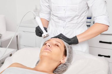 Güzellik uzmanı, güzellik salonundaki yaşlanma önleyici kozmetik işlemleri ve fonoforezi kullanarak gençleşen kadın yüzü için ultrason cildi sıkılaştırıyor. Kozmetik uzmanı ultrasonik deri kaldırıyor.