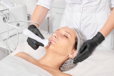 Kozmetik uzmanı, güzellik salonundaki yaşlanmayı önleyen kozmetik prosedürleri kullanarak gençleşen kadın yüzü için ultrason cildini sıkılaştırıyor. Güzellik uzmanı ultrasonik deri kaldırıyor.