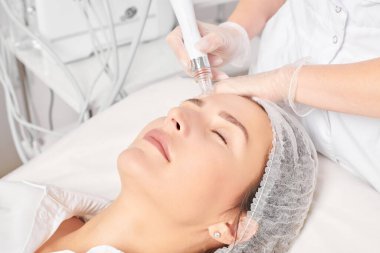 Güzellik uzmanı, güzellik salonundaki yaşlanma karşıtı kozmetik prosedürü olan cilt bakımını yenilemek için su bitkisi üretiyor. Eldivenleri teslim eden kozmetolog, sıkılaştırmak için yüz bakımı yapıyor