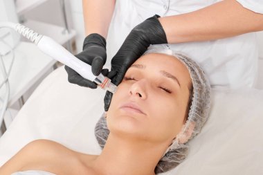 Güzellik uzmanı, güzellik salonundaki yaşlanma karşıtı kozmetik prosedürü olan cilt bakımını yenilemek için su bitkisi üretiyor. Siyah eldivenleri teslim eden kozmetolog, sıkılaştırmak için yüz bakımı yapıyor