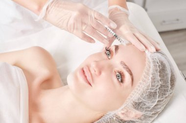Kozmetik uzmanı kadın yüzüne gençleştirme enjeksiyonu yapıyor. Güzellik salonunda yaşlanmayı önleyen estetik cerrahi olmayan prosedür uyguluyor. Eldiven uzmanları şırınga ile iğne yapıyor.
