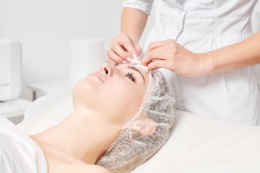 Güzellik uzmanı, güzellik salonundaki yüz kremi maskesini kadın yüzünden kozmetik mendillerle alıyor, cilt yenileme estetik ameliyatı yapıyor. Kozmetik uzmanı yüz maskesini çıkarmak için peçete tutuyor.