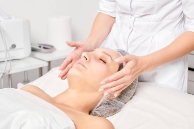 Güzellik uzmanları, güzellik salonlarında gençleştirme için nemlendirici krem maskeyi kadın yüzüne sürerler, yaşlanma karşıtı kozmetik işlemler yaparlar. Kozmetik uzmanı kadın derisi için yüz kremi uyguluyor.