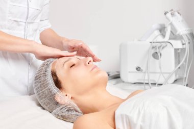 Güzellik uzmanları, güzellik salonlarında gençleştirme için nemlendirici krem maskeyi kadın yüzüne sürerler, yaşlanma karşıtı kozmetik işlemler yaparlar. Kozmetik uzmanı kadın derisi için yüz kremi uyguluyor.