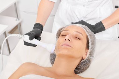 Kozmetik uzmanı, güzellik salonundaki gençleşen kadın yüzü için RF kaldırma, yaşlanma karşıtı kozmetik prosedürü yapıyor. Güzellik uzmanı kadın yüz derisinde artan kolajen için radyo frekansı tedavisi uyguluyor.