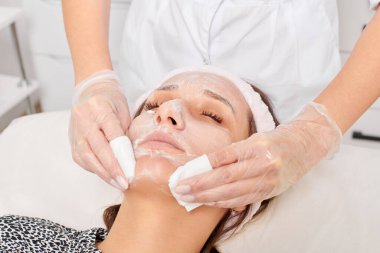 Güzellik uzmanı, güzellik salonundaki yüz kremi maskesini kadın yüzünden kozmetik mendillerle alıyor, cilt yenileme estetik ameliyatı yapıyor. Kozmetik uzmanı nemlendirici kremi peçetelerle temizliyor.