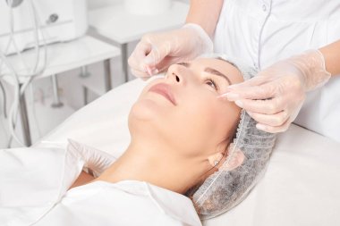 Kozmetik uzmanı güzellik salonundaki gençleştirme, yaşlanmayı önleyici kozmetik prosedürler için kadın yüzüne yüz yağı kapsülleri uyguluyor. Eldivenli güzellik uzmanı beslenme için yağ kapsülleri tutuyor.