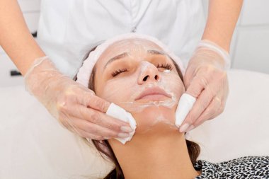 Güzellik uzmanı, güzellik salonundaki yüz kremi maskesini kadın yüzünden kozmetik mendillerle alıyor, cilt yenileme estetik ameliyatı yapıyor. Kozmetik uzmanı nemlendirici kremi peçetelerle temizliyor.