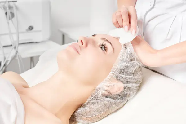 Cosmetologist making facial massage with Gua Sha stone of woman face skin for lymphatic drainage, anti aging skincare cosmetic procedure in beauty spa salon. Face massage with Gua Sha tool
