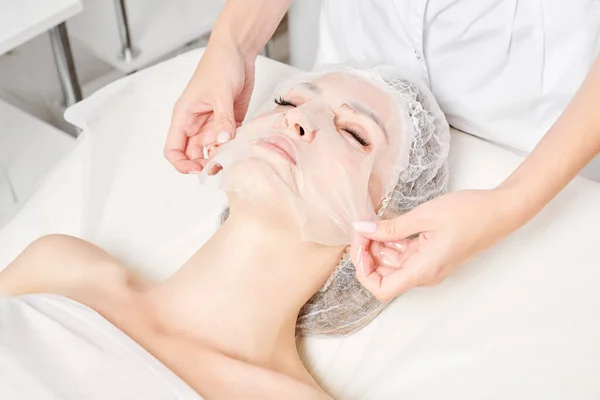 Beautician Smoothes Sheet Mask Pada Wanita Wajah Untuk Kulit Wajah — Stok Foto