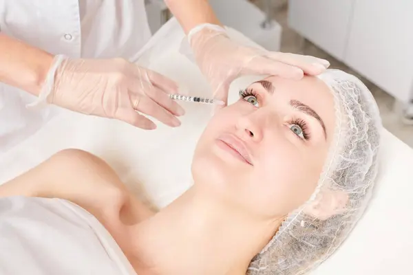 Cosmetologist makes rejuvenation injection in woman face, anti aging non surgical cosmetic procedure in beauty salon. Beautician specialist hands in gloves makes treatment injection with syringe