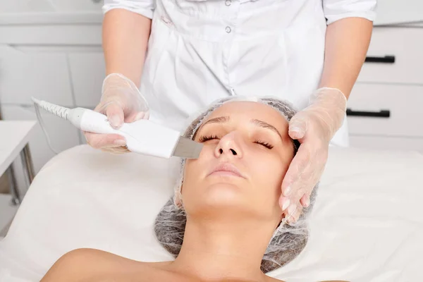 Beautician makes facial ultrasonic peeling for rejuvenation woman face skincare, anti aging cosmetic procedure in beauty spa salon. Cosmetologist makes face skin treatment with ultrasound scrubber