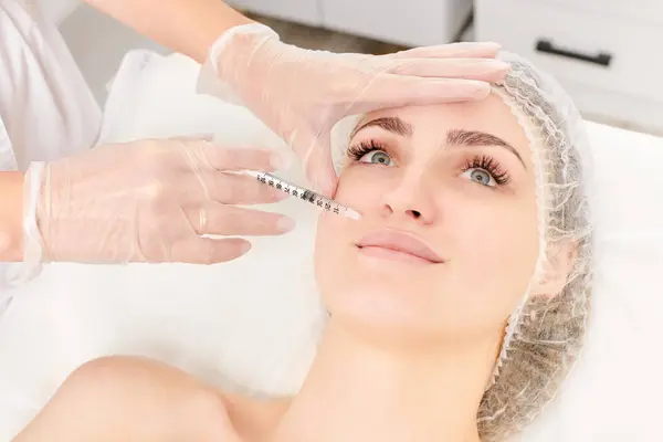 Cosmetologist makes fillers injection for lips augmentation and volume, non surgical cosmetic procedure in beauty salon. Beautician specialist hands in gloves makes treatment injection with syringe
