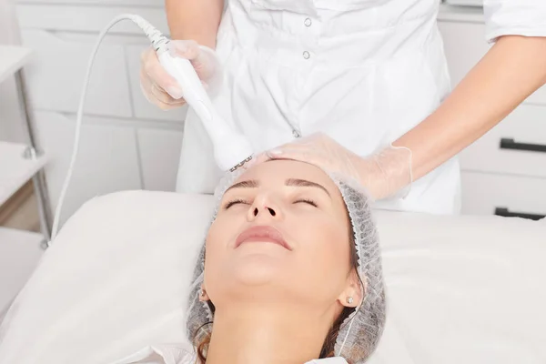 美容师使射频升华对年轻化妇女的面容 美容院的抗衰老美容美发具有重要作用 美容师对女性面部皮肤胶原蛋白增加进行射频治疗 — 图库照片