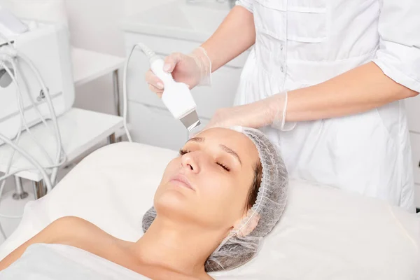 Beautician makes facial ultrasonic peeling for rejuvenation woman face skincare, anti aging cosmetic procedure in beauty spa salon. Cosmetologist makes face skin treatment with ultrasound scrubber