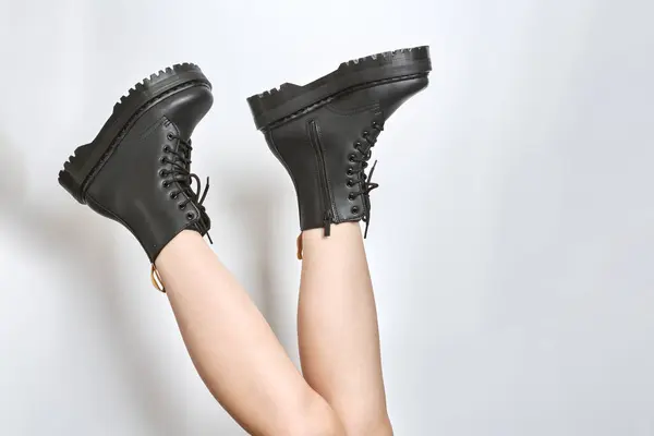 Woman legs in black combat boots on high heel platform with lug soles upside down side view on isolated white background. Female legs wear military fashionable high heel platform combat boots