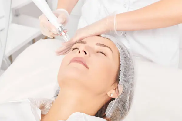 Cosmetologist makes aqua exfoliation for rejuvenation woman face skincare, anti aging cosmetic procedure in beauty spa salon. Beautician hands in gloves makes face skin treatment for tightening